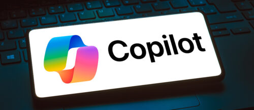 Bildbeschreibung: Das Bild zeigt einen Smartphone-Bildschirm mit dem Logo und dem Text "Copilot" in fetter Schrift, begleitet von einem bunten Symbol, platziert auf einer Laptop-Tastatur.