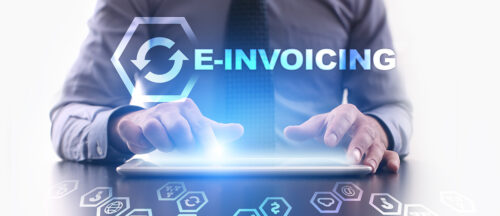 Bildbeschreibung: Das Bild zeigt einen Geschäftsmann, der auf einem Tablet arbeitet, mit einem leuchtenden Symbol für elektronische Rechnungen (E-Invoicing) im Vordergrund.